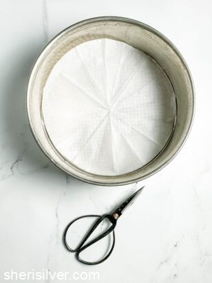 parchment paper circle in a round pan next to vintage scissors