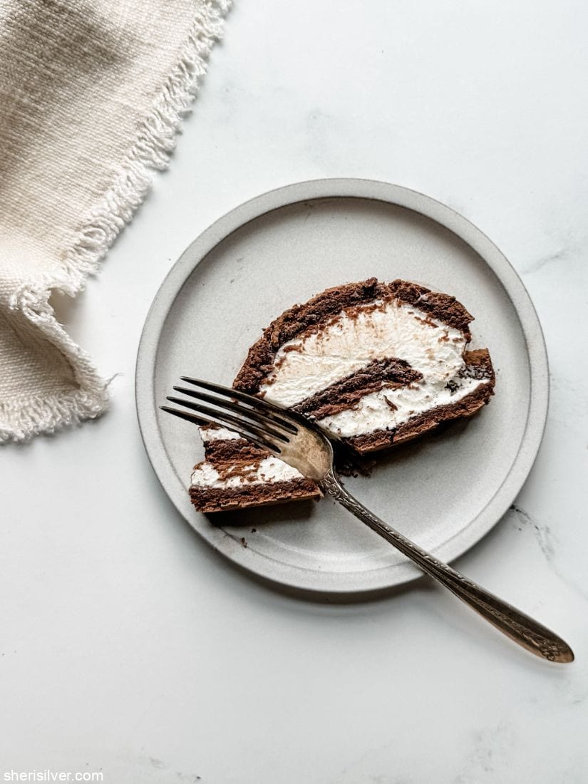 flourless chocolate roulade on a white ceramic plate next to a fringed linen napkin