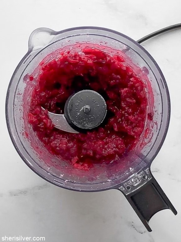 Finely chopped cranberries mixed with vanilla sugar in food processor bowl.
