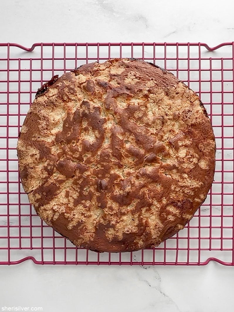 Golden cake cooling on a pink rack, topped with crisp crumb and ready to serve.