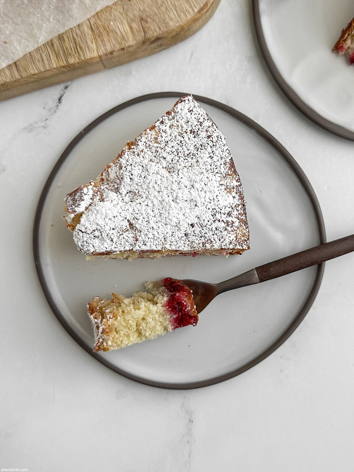 Overhead close-up of a slice of cranberry vanilla coffee cake with a forkful of cake beside it, showing the moist crumb and cranberry swirl.