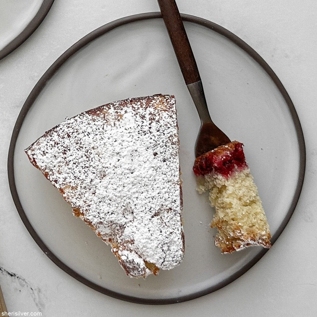 Overhead close-up of a slice of cranberry vanilla coffee cake with a forkful of cake beside it, showing the moist crumb and cranberry swirl.