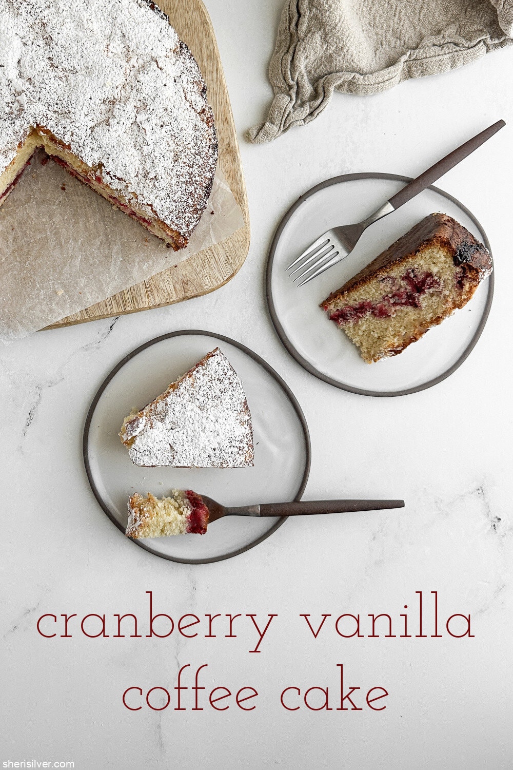 Overhead view of two slices of cranberry vanilla coffee cake on white plates with silver forks, one upright and one on its side with a forkful of cake.
