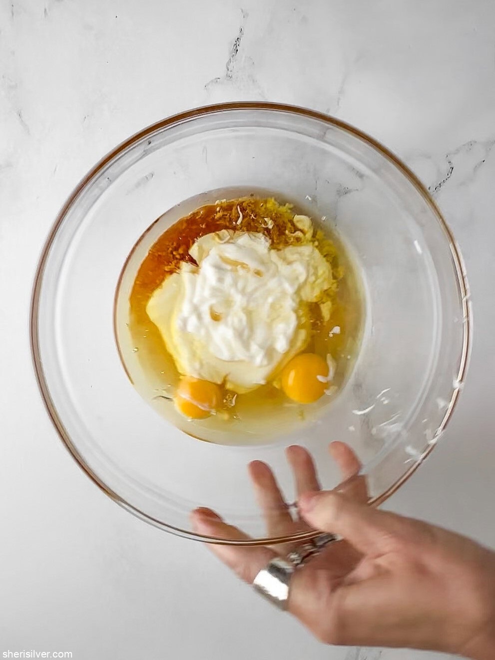 Olive oil, eggs, honey, yogurt, lemon juice, zest, and vanilla in a glass bowl for honey lemon yogurt cake.