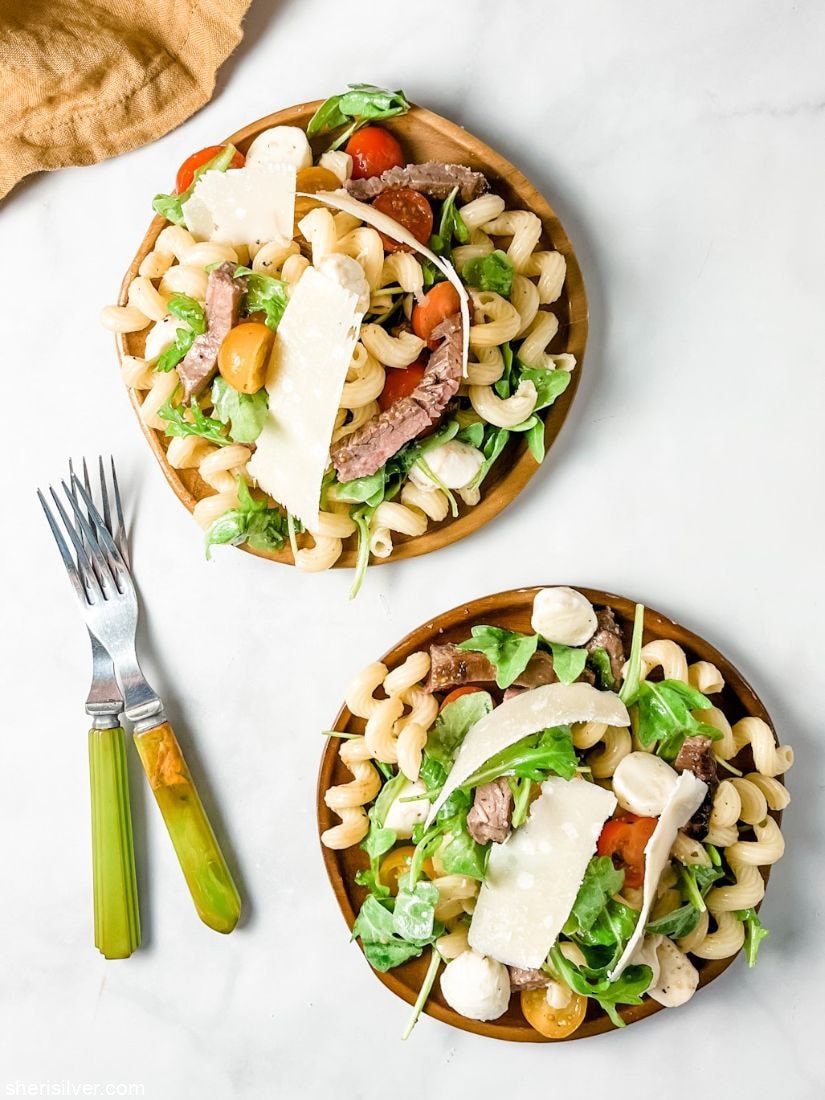 steak pasta salad on wooden plates next to a linen napkin