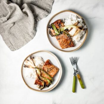 broiled salmon with scallions on white plates with green forks and striped linen napkin