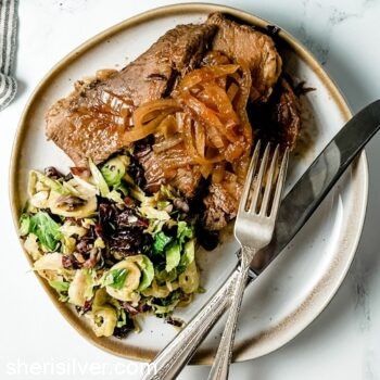 brisket with brussels salad on a ceramic plate with vintage silverware
