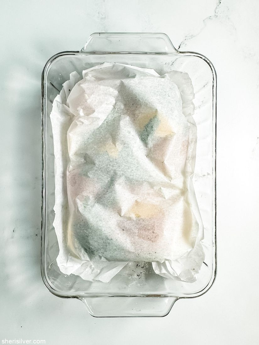 chicken breasts in a glass baking dish covered with parchment paper