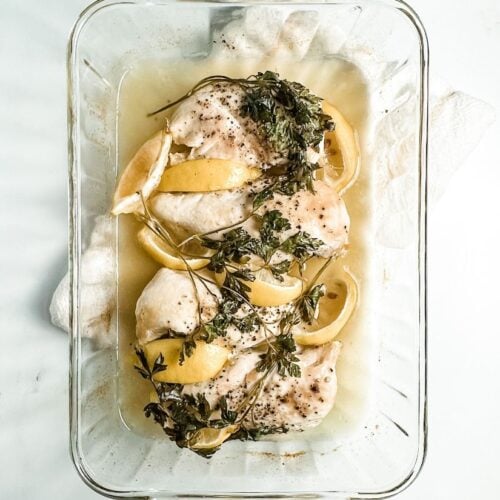 oven baked chicken breasts with lemon and parsley in a glass baking dish