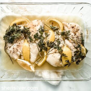 oven baked chicken breasts with lemon and parsley in a glass baking dish