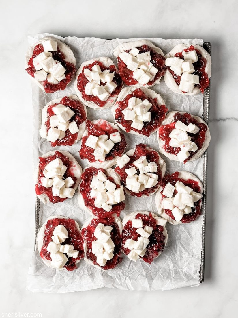 biscuits layered with cranberries and brie on a parchment lined baking sheet