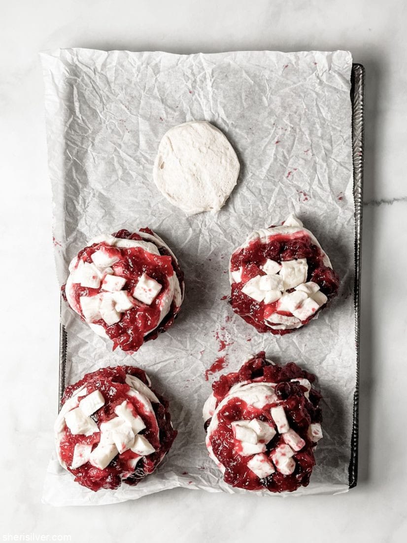 biscuits layered with cranberries and brie on a parchment lined baking sheet