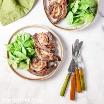 beef pinwheels with arugula salad on white plates with vintage cutlery and green linen napkin