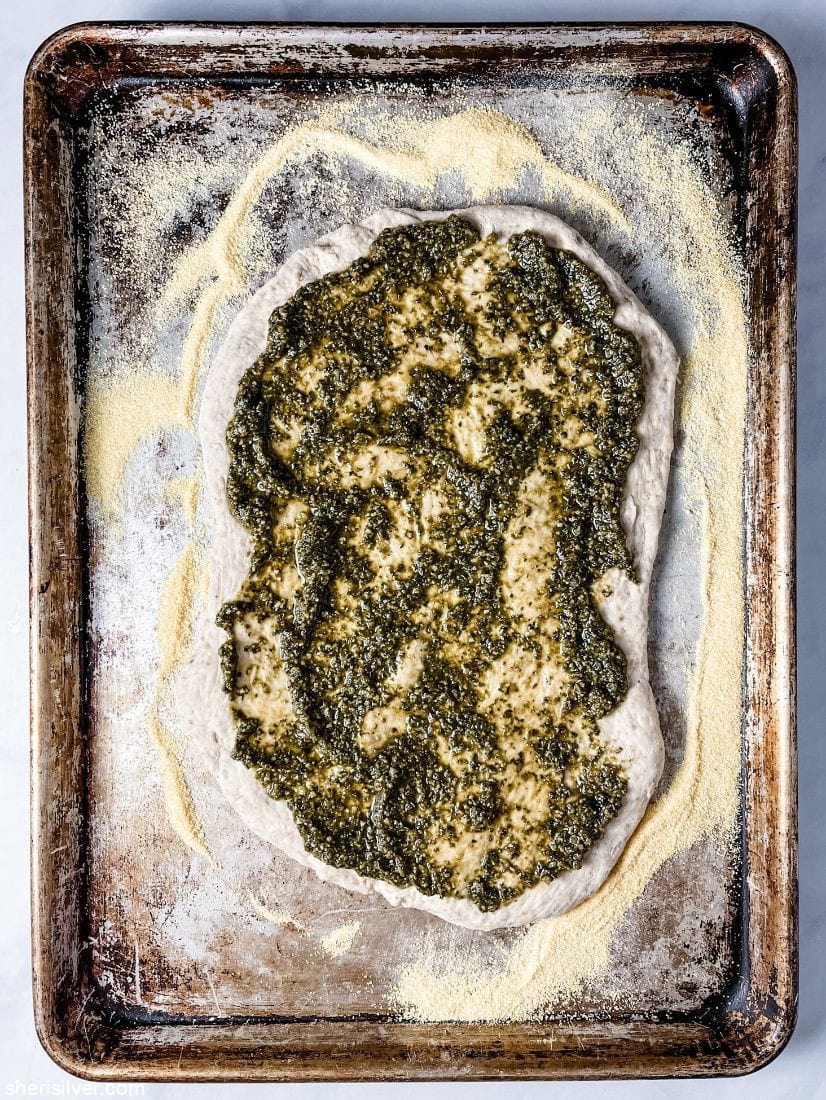 pizza dough on a sheet pan topped with pesto