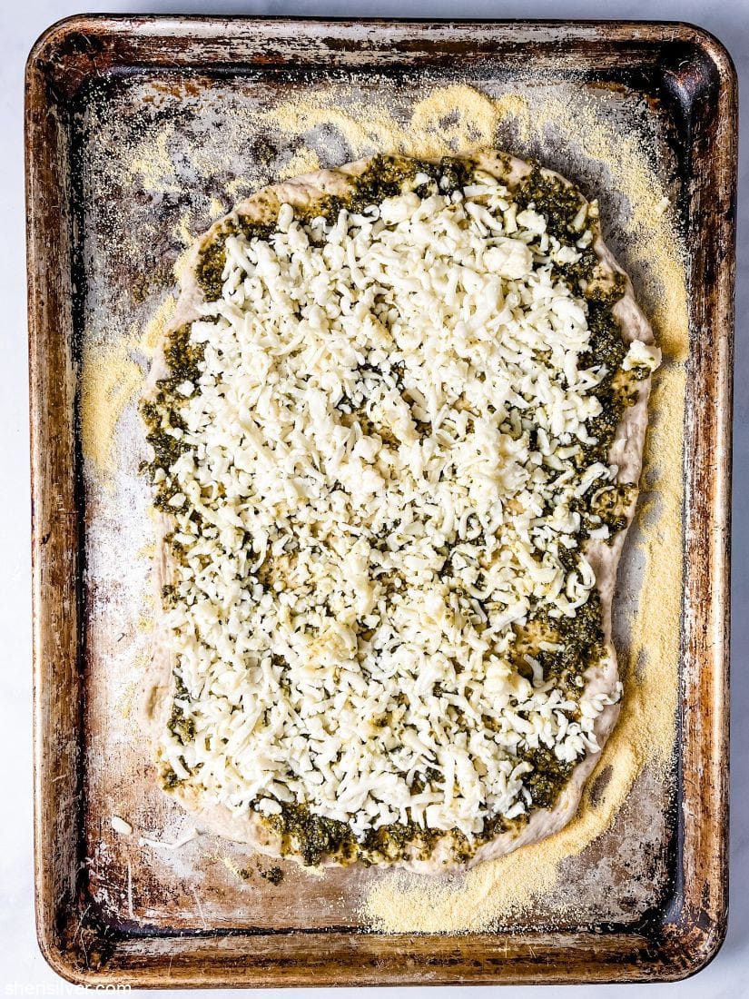 pizza dough on a sheet pan topped with pesto and mozzarella