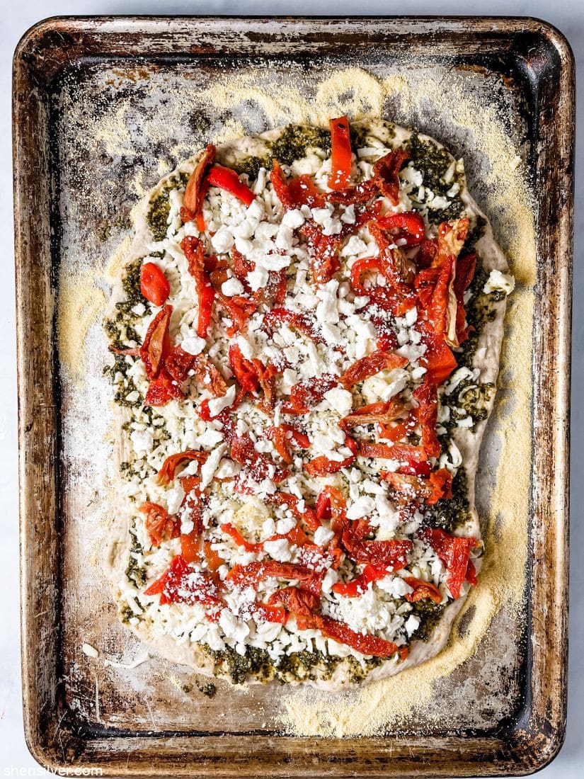pizza dough on a sheet pan topped with roasted peppers and sundried tomatoes