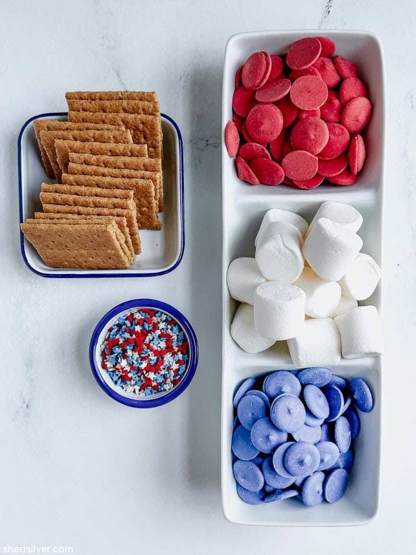 white trays filled with red candy melts marshmallows blue candy melts graham crackers and star sprinkles