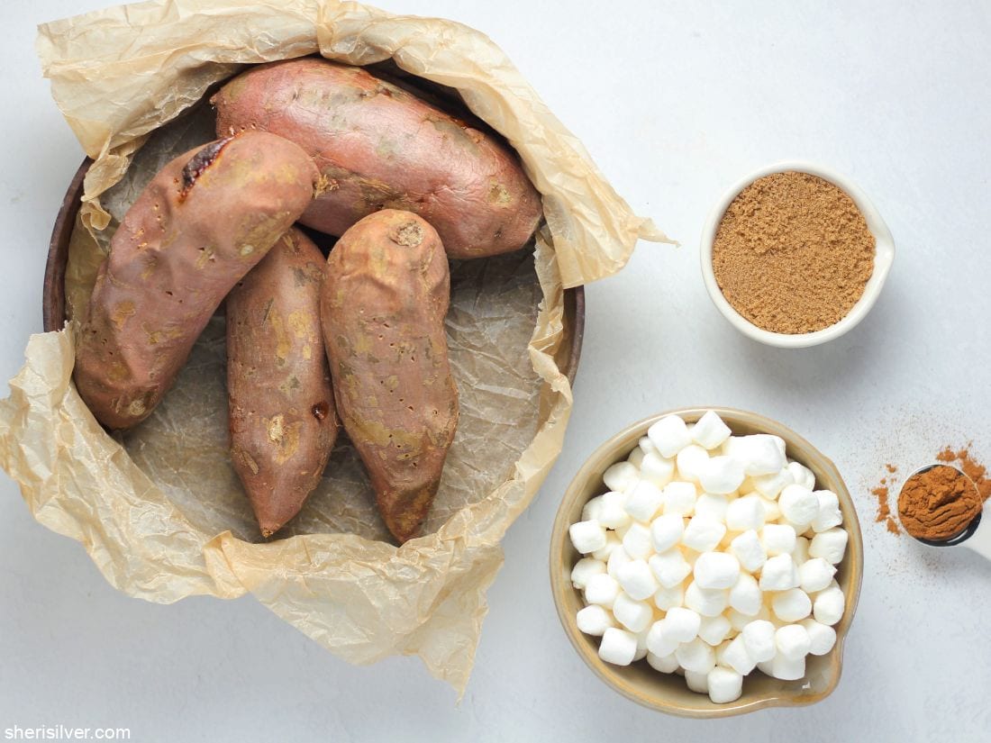sweet potatoes in a parchment lined metal pan next to dishes of brown sugar and mini marshmallows