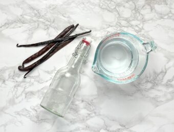 vanilla beans next to a glass bottle and pyrex measuring cup
