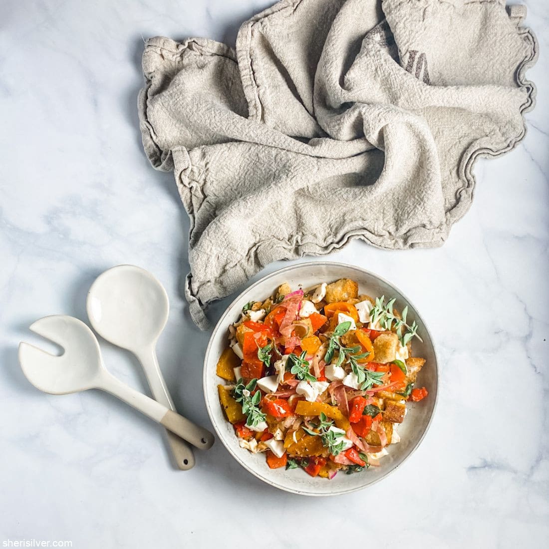 roasted pepper panzanella in a ceramic bowl with serving fork and spoon and linen napkin