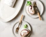 gluten free meringue roll on white plates with vintage forks next to striped kitchen towel