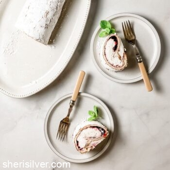 gluten free meringue roll on white plates with vintage forks next to striped kitchen towel