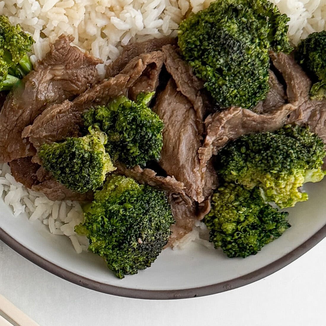 Close-up overhead view of velveted beef and broccoli with white rice in a bowl showing the silky tender texture of the beef