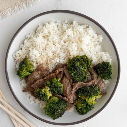 Overhead view of a single bowl of velveted beef and broccoli with white rice and chopsticks on marble