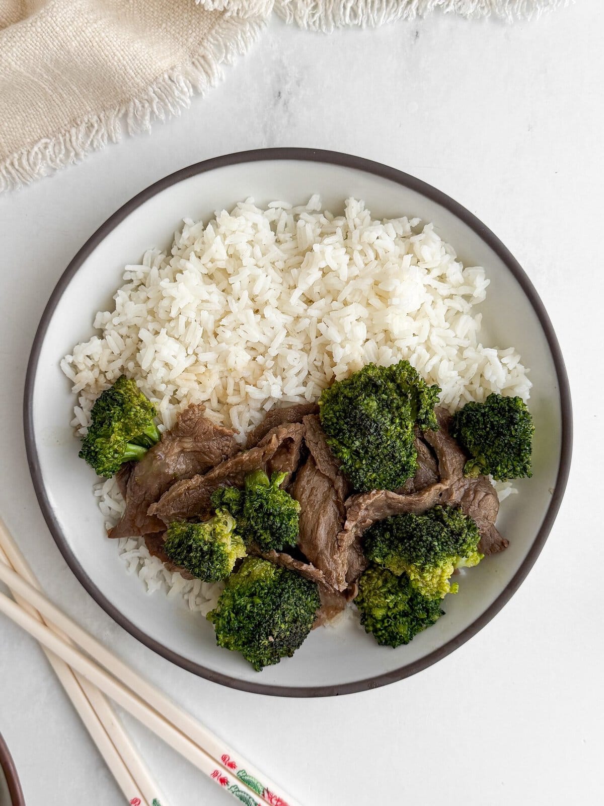 Overhead view of a single bowl of velveted beef and broccoli with white rice and chopsticks on marble