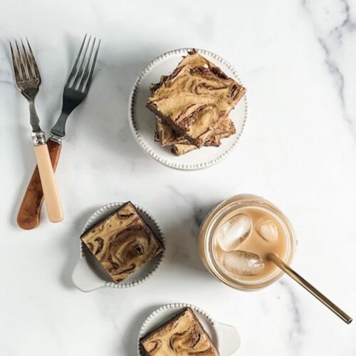 mocha cheesecake brownies on ceramic plates with iced coffee in a mason jar