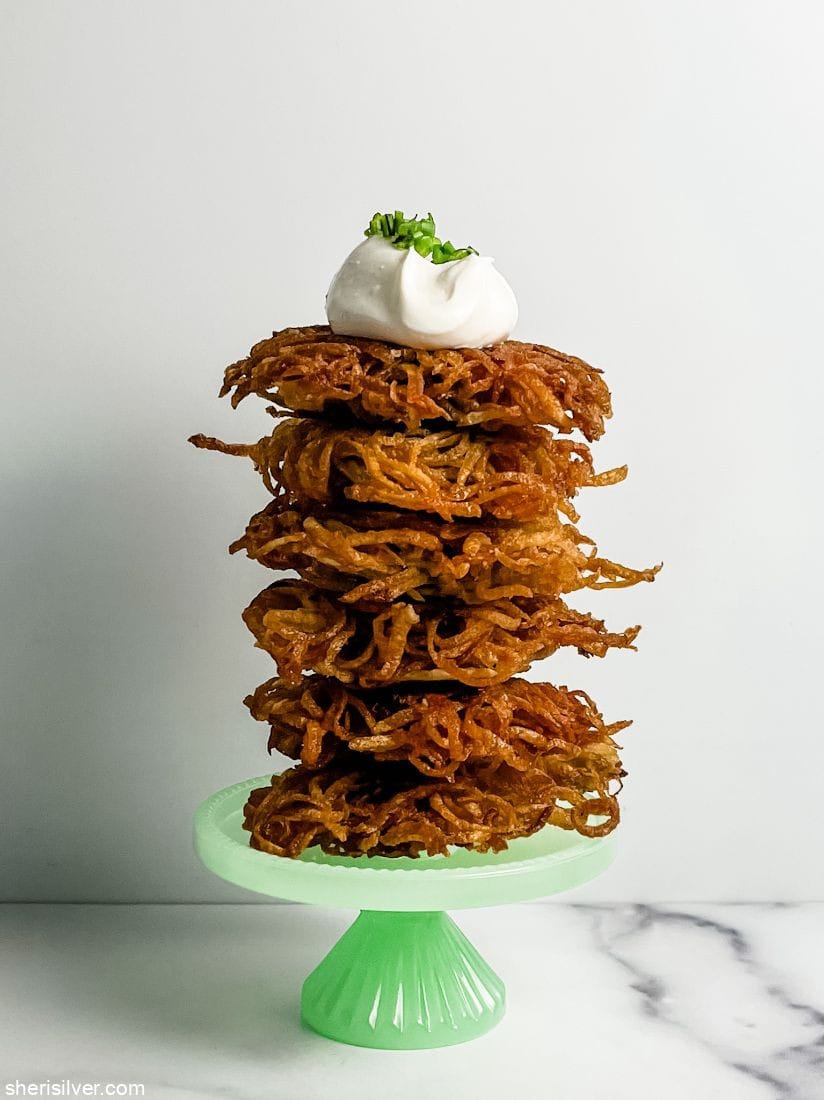 potato latkes stacked on a cake stand and topped with sour cream and chives