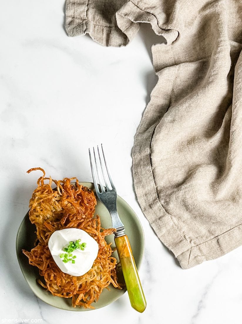 potato latkes stacked on a plate and topped with sour cream and chives