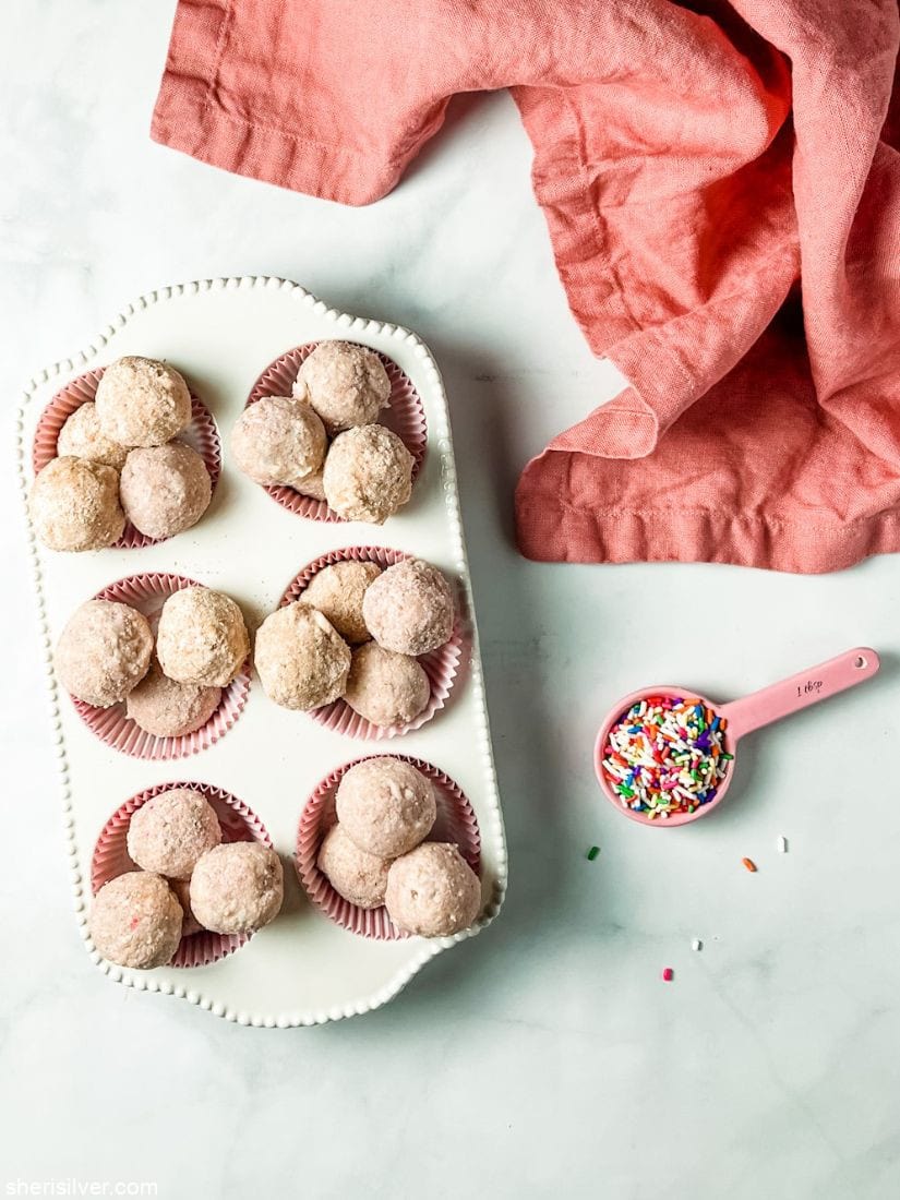 milk bar birthday cake truffles in a white ceramic muffin tin with pink spoonful of rainbow sprinkles