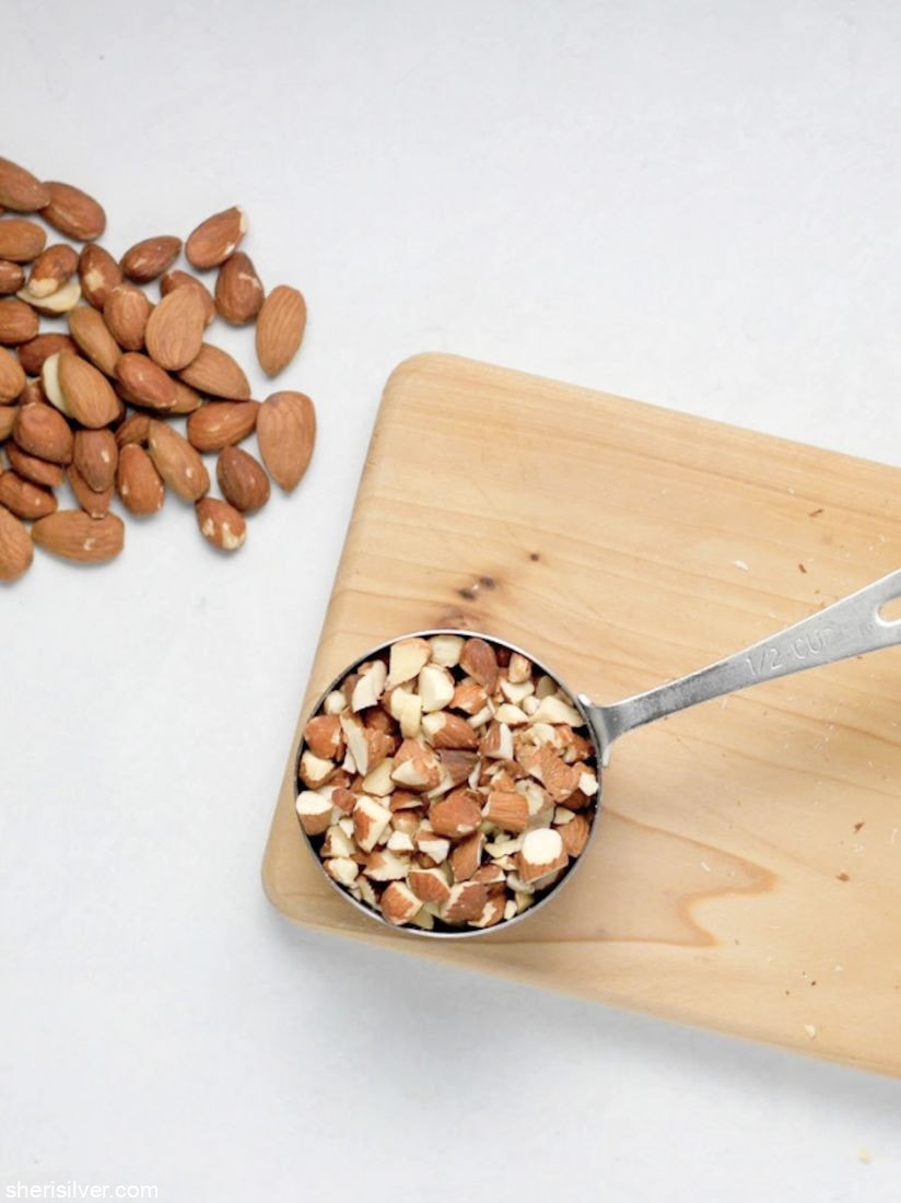 chopped almonds in a measuring cup on a wooden board next to whole almonds