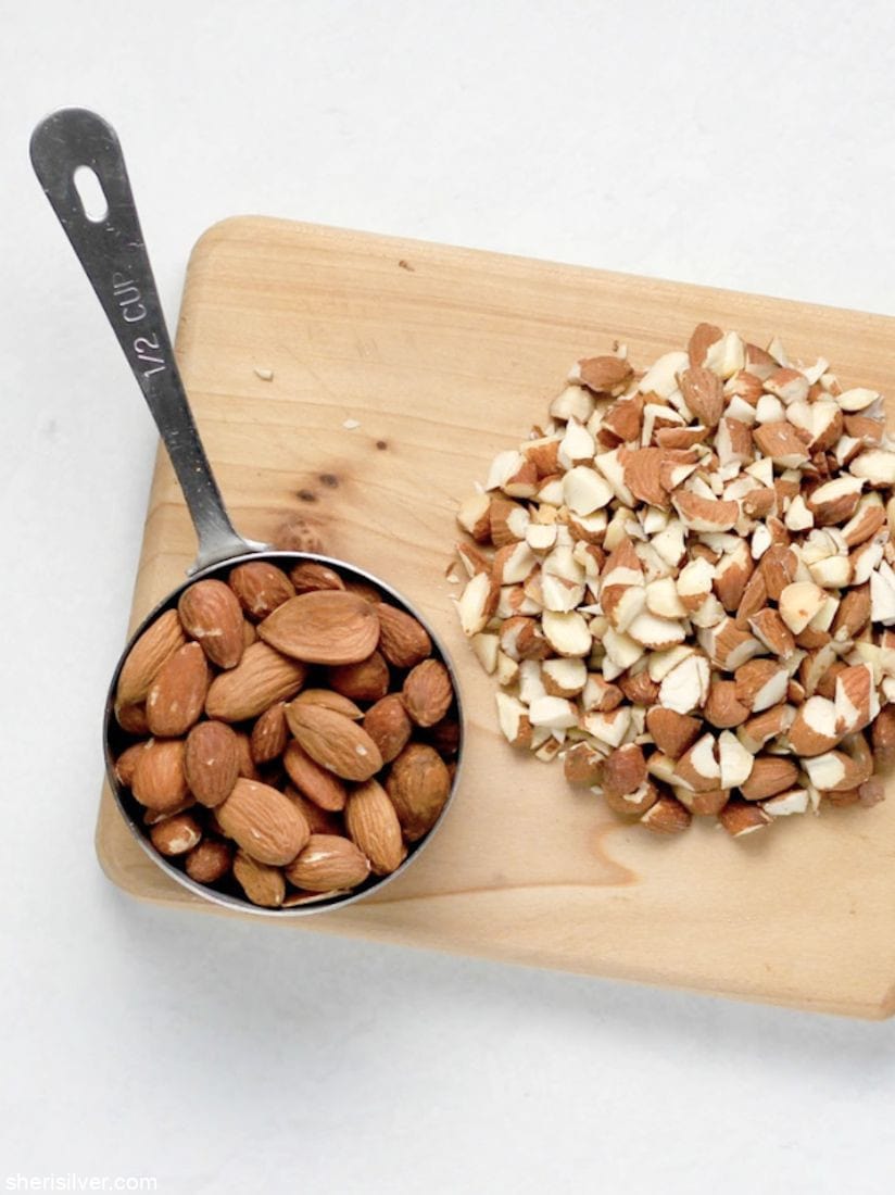 whole almonds in a measuring cup on a wooden board next to whole almonds