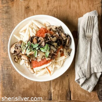 pasta with mushrooms and tomatoes in a ceramic bowl on a wooden board