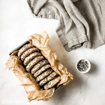 tahini stuffed sugar cookies in a parchment lined loaf pan next to a dish of sesame seeds