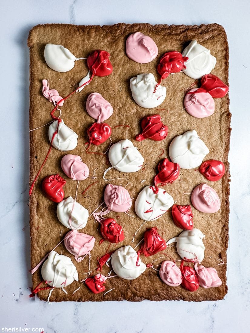 dollops of white pink and red candy melts atop a sheet pan cookie