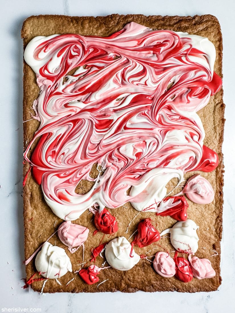 pink white and red candy melts swirled atop a sheet pan cookie