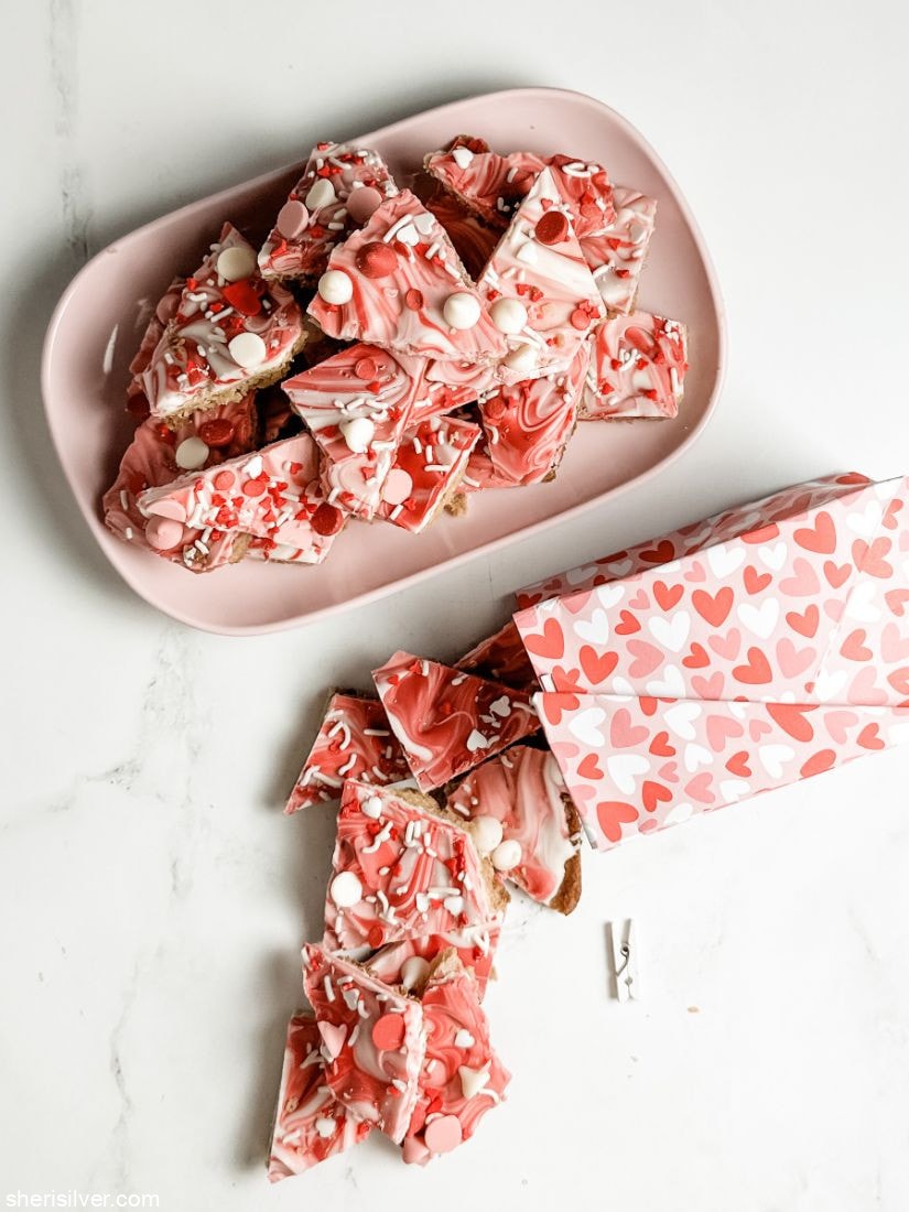 valentine cookie bark on a pink plastic tray nest to a paper bag filled with valentine cookie bark