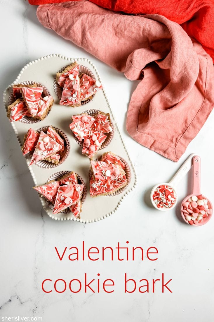 valentine cookie bark in a ceramic muffin tin next to ceramic spoons filled with valentines sprinkles