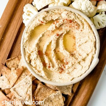 hummus on a wooden board with pita chips and crudite
