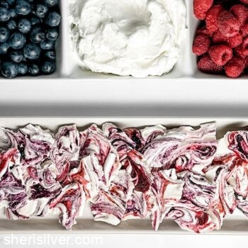 berries and whipped cream in a divided ceramic tray next to a tray of berry meringue bark