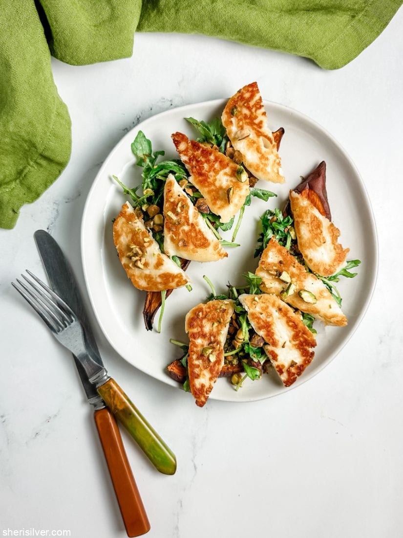 sweet potato toasts topped with arugula and halloumi on a white plate next to vintage flatware