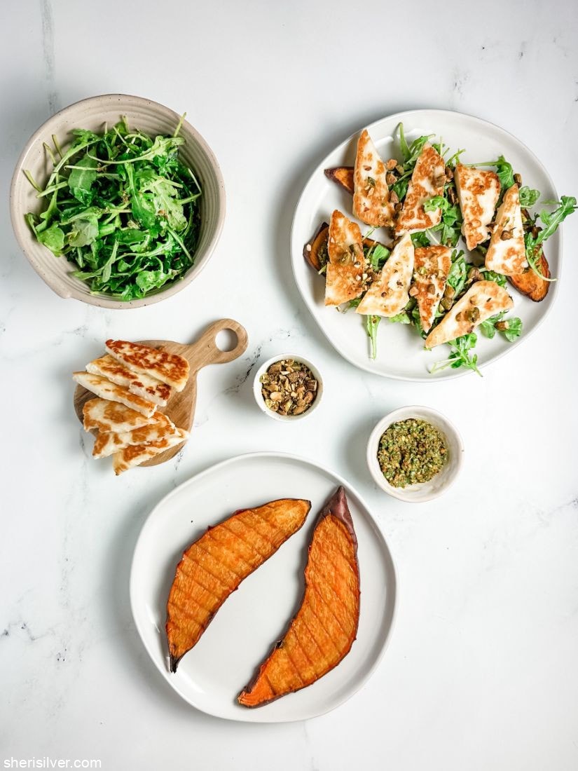 sweet potato toasts topped with arugula and halloumi on a white plate next to a plate of roasted sweet potato slices