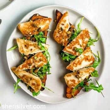 sweet potato toasts topped with arugula and halloumi on a white plate
