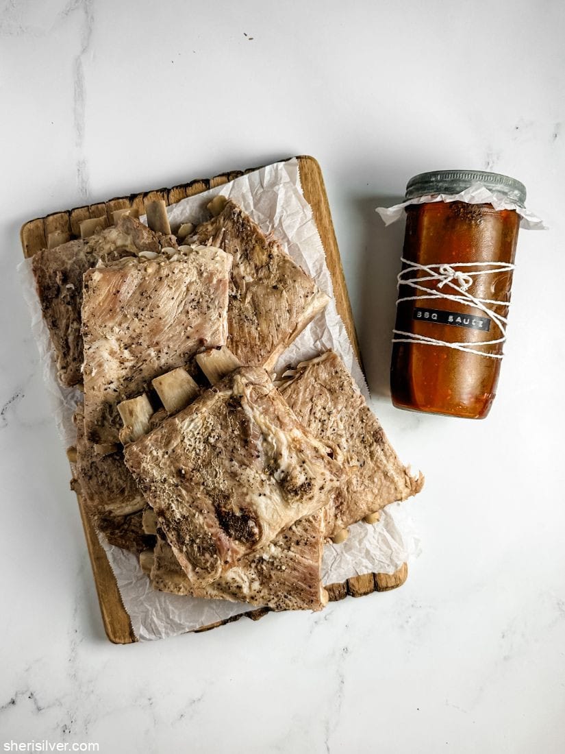 grilled ribs on a wooden board next to a mason jar filled with bbq sauce