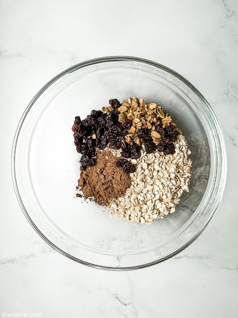 cocoa powder in a glass mixing bowl with oats pistachios and dried cherries
