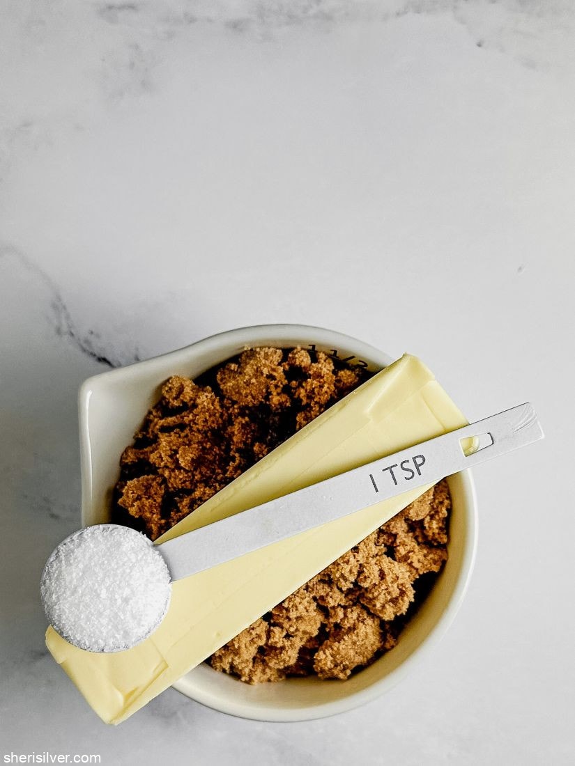 a teaspoon of salt on top of a stick of butter on top of a cup of brown sugar