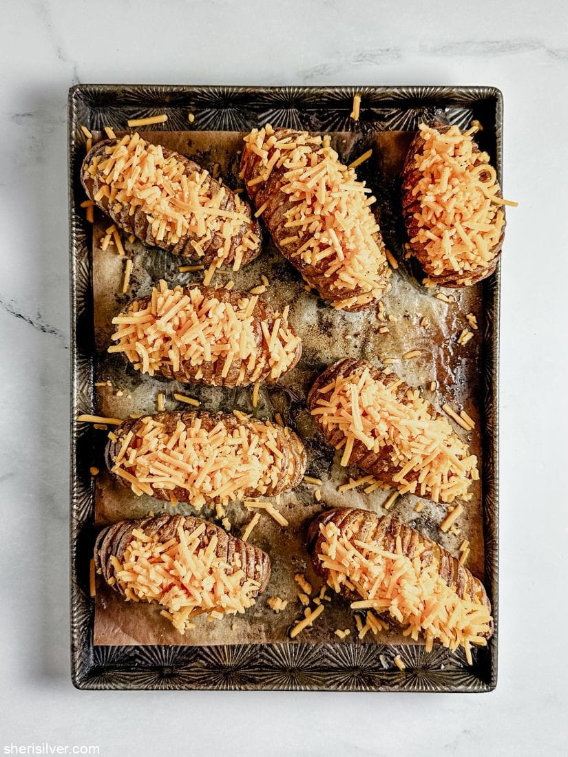 hasselback potatoes topped with shredded cheese on a parchment lined baking sheet
